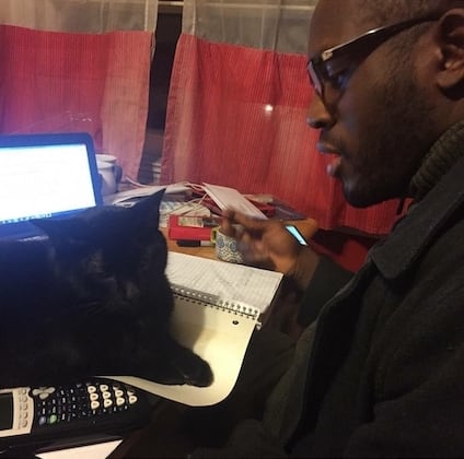 Photo of Ed Latimore studying physics, with his cat sitting on a stack of papers in front of him